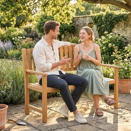 Man en vrouw zitten lachend op een houten tuinbank in een zonnige tuin.