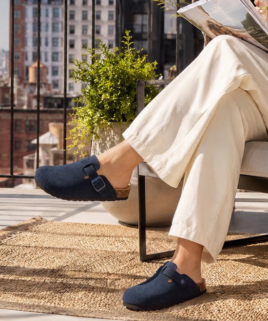 Vrouw op balkon met beige broek en donkerblauwe klompen met suède-look.