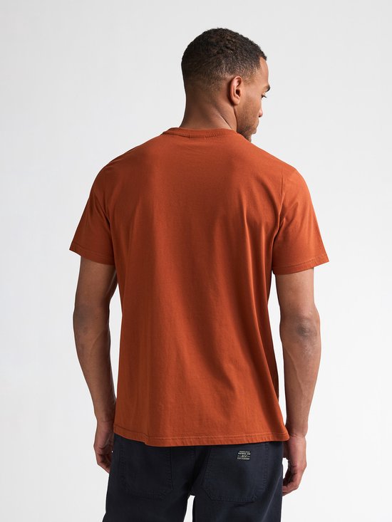 Model van achteren gezien in een oranje t-shirt met korte mouwen en navy broek.