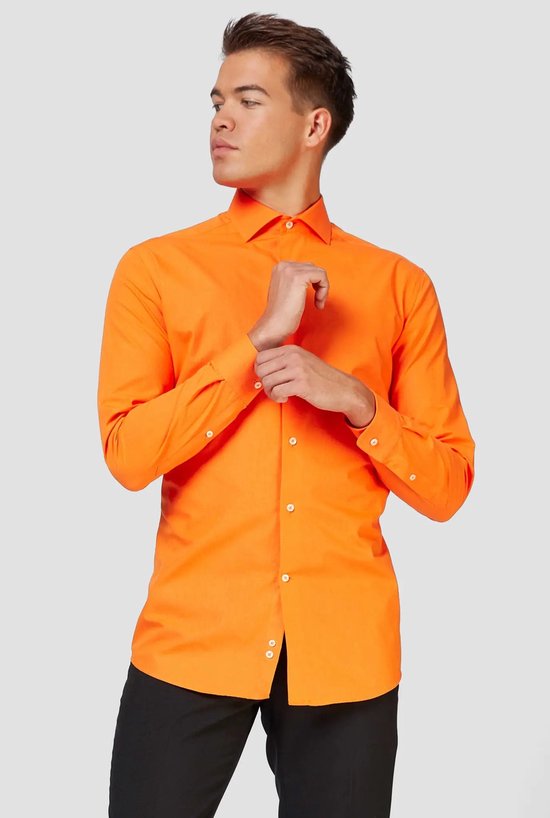 Homme en chemise orange à manches longues et boutons blancs, ajustant son poignet.