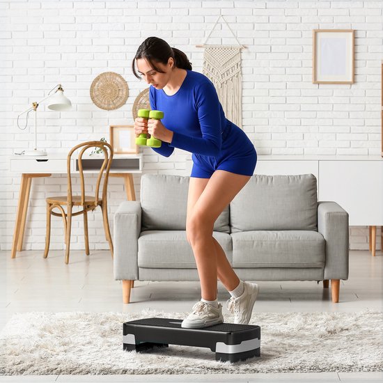 Vrouw in sportkleding traint met dumbbells op een zwarte step met witte accenten.