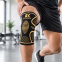 Zwarte KANGKA kniebrace met gouden accenten, honingraatpatroon en ovaal met strepen. Een man draagt de brace tijdens het sporten.