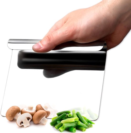 Een hand houdt een metalen deegschraper vast boven gesneden champignons en sperziebonen, met een witte achtergrond.