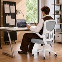 Een man zit op een grijze bureaustoel met witte armleuningen en een wit onderstel aan een bureau te werken, met een laptop.