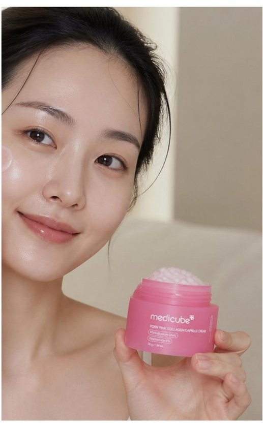 Jonge Aziatische vrouw met een stralende huid, houdt een Medicube PDRN Pink Collagen Capsule Cream vast.
