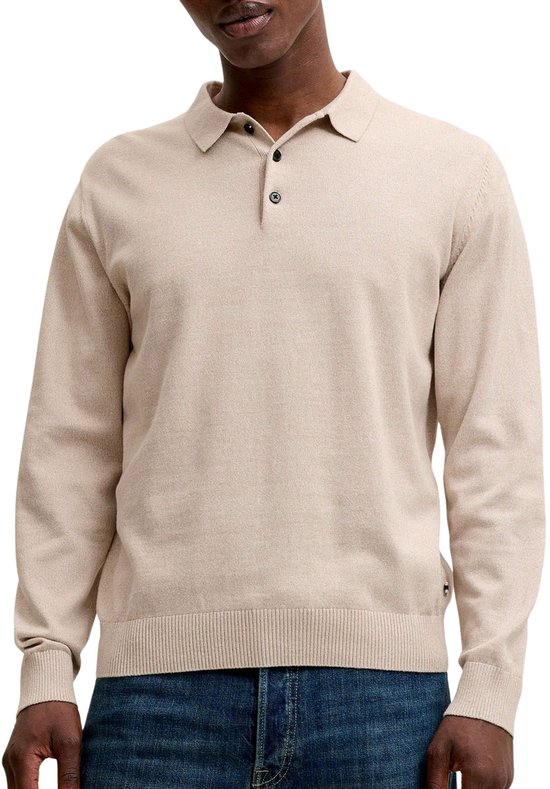 Man, lichtbeige gebreid poloshirt met lange mouwen, twee zwarte knoopjes en donkerblauwe jeans.