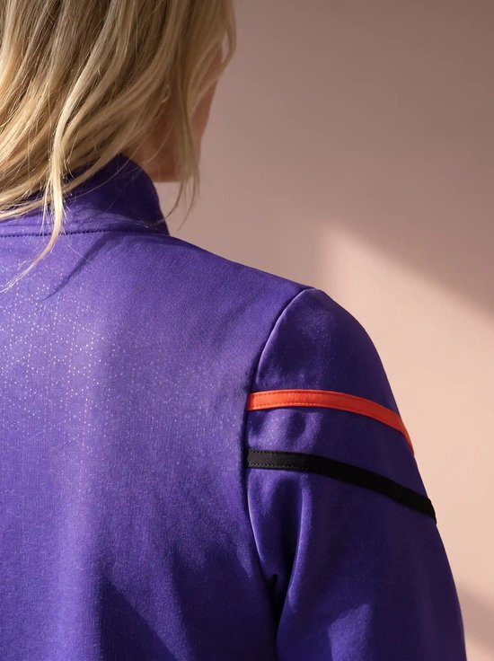 Detail van een paars sportvest met een lichte textuur en oranje en zwarte strepen op de schouder.
