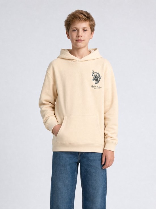 Jongen in crèmekleurige hoodie, blauwe jeans, met kraan-print op de borst en tekst 'Built to Endure'.
