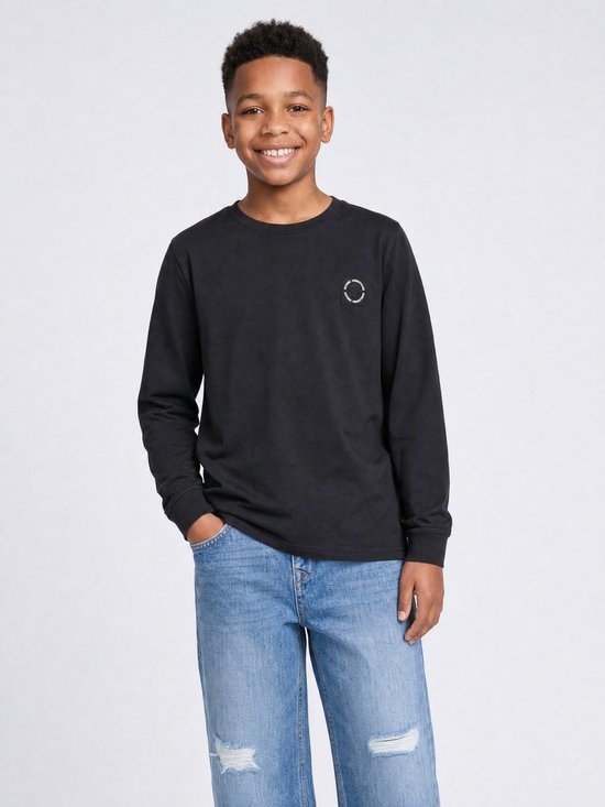 Jongen met een zwarte longsleeve en distressed jeans.