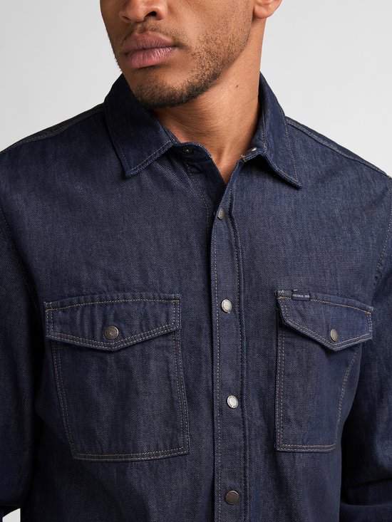 Detail van een donkerblauw denim overhemd met twee borstzakken, knopen en Petrol Industries logo.