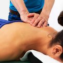 Massage van de schouder door een persoon met blauw shirt.