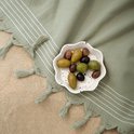 Een schaaltje olijven op een groene hamamdoek met witte strepen en franjes, op zand.