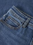 Close-up van de blauwe jeans met zakdetails en bruine stiksels.