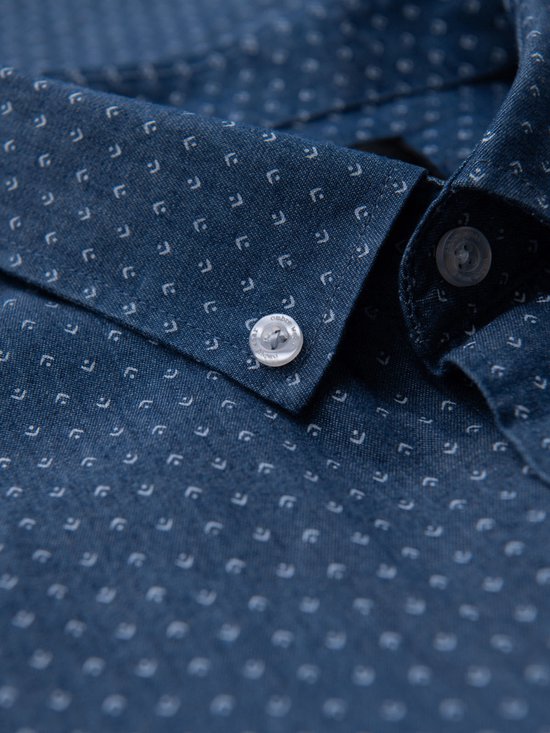 Close-up van de kraag en knoop van een blauw overhemd met witte stipjes.