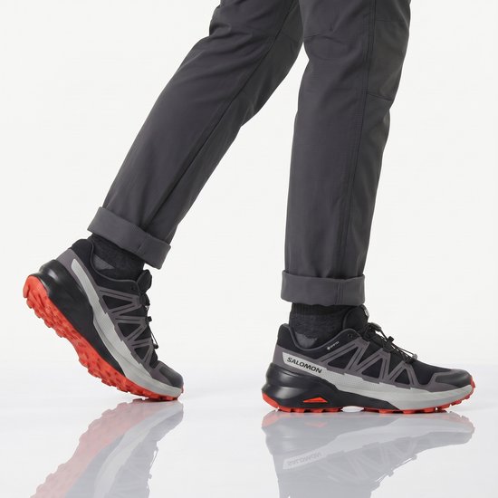 Man die loopt in zwarte Salomon trailrunningschoenen met grijze en oranje details.