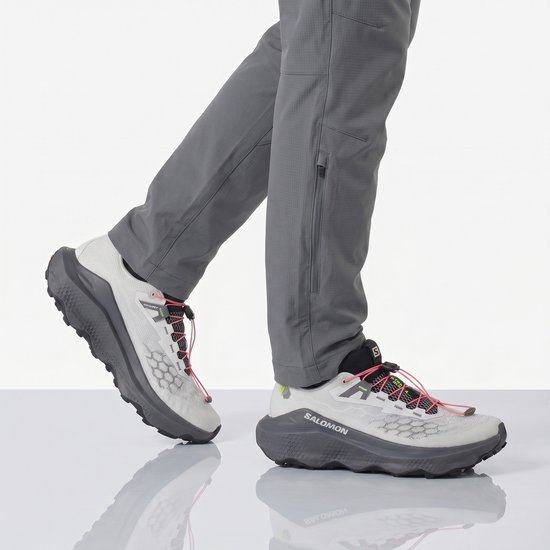 Grijze Salomon trailrunningschoenen met roze veters, gedragen door een model.