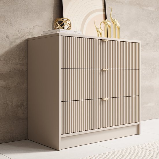 Commode beige à trois tiroirs, texture côtelée verticale et poignées dorées.