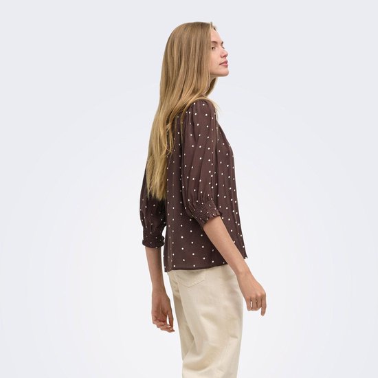 Bruine blouse met witte stippen en driekwart mouwen, gedragen door een model.
