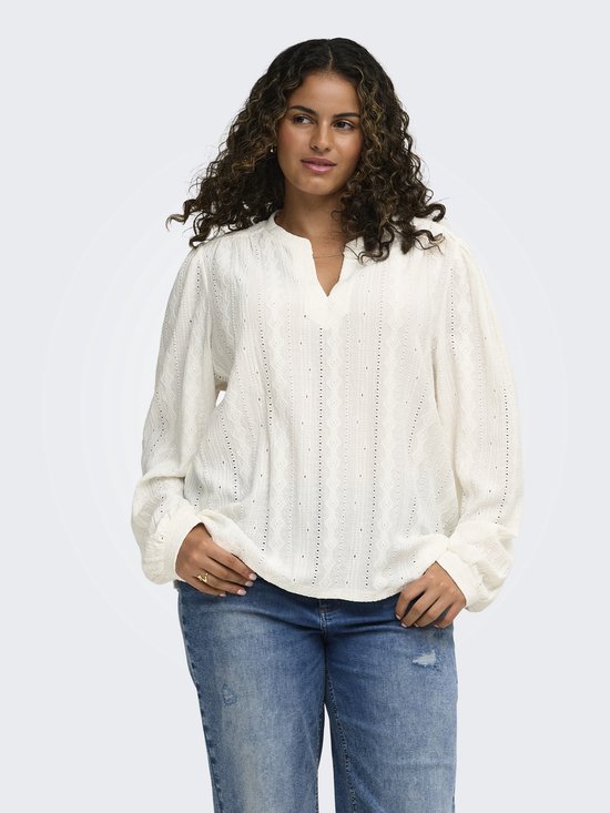 Model draagt crèmekleurige blouse met V-hals, lange pofmouwen en geometrisch patroon, gecombineerd met jeans.