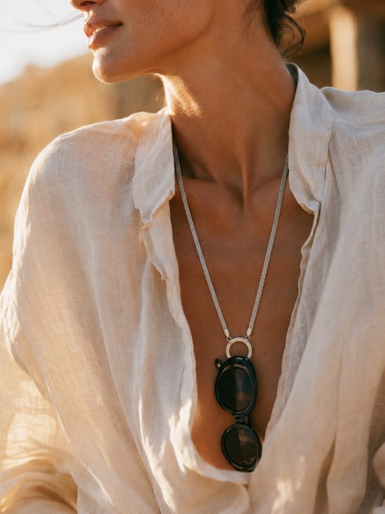 Model met zilverkleurige ketting met ronde hanger en zwarte zonnebril.