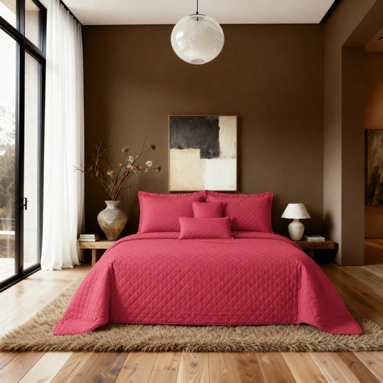 Bed opgemaakt met een rode, doorgestikte sprei en bijpassende kussenslopen in een slaapkamer.
