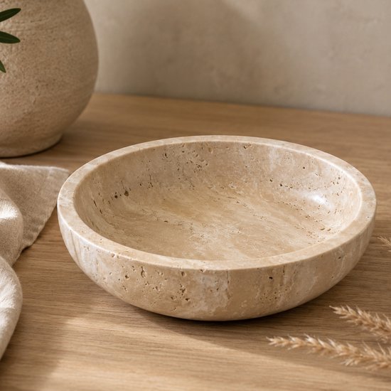 Beige travertin schaal met natuurlijke aders, op een houten tafel met linnen doek.