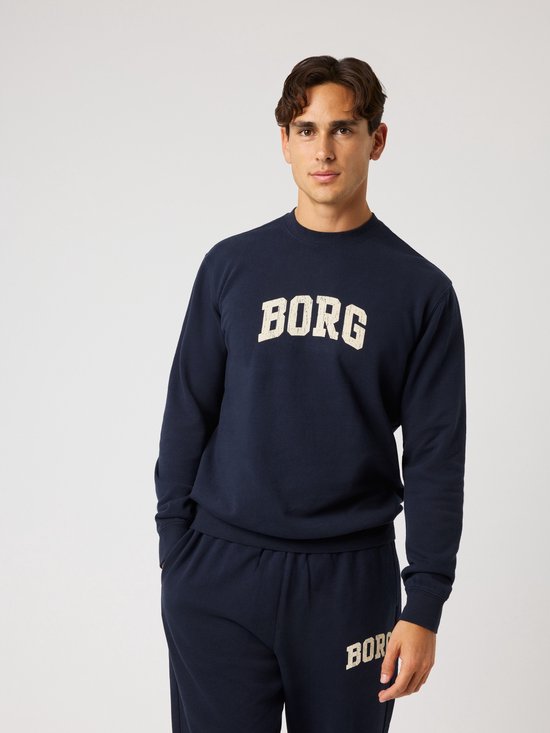 Man draagt een donkerblauwe sweater met beige 'BORG' opdruk en een bijpassende joggingbroek.