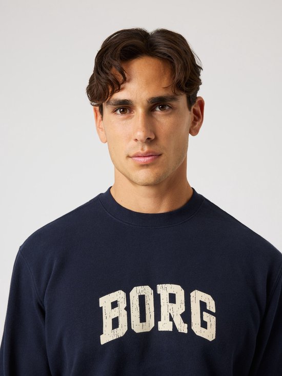Donkerblauwe sweater met beige 'BORG' opdruk op de borst. Model draagt de sweater.