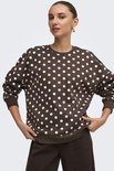 Model draagt een bruine sweater met witte polkadots, gecombineerd met een bruine broek.
