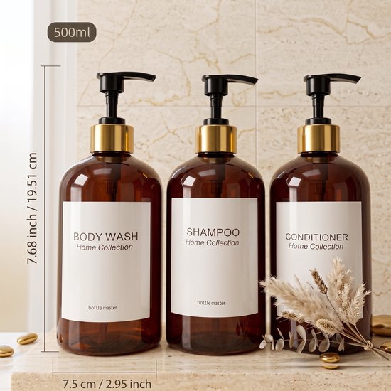 Drie amberkleurige pompflessen met gouden accenten, labels voor Body Wash, Shampoo en Conditioner, op een marmeren aanrecht.