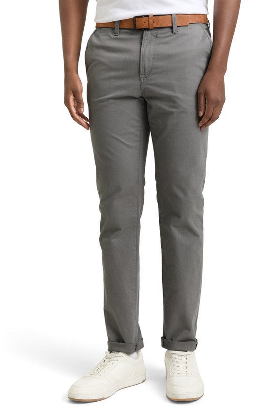 Man in grijze chino met bruine riem, opgerolde pijpen en witte sneakers.