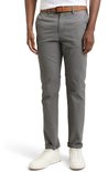 Man in grijze chino met bruine riem, opgerolde pijpen en witte sneakers.