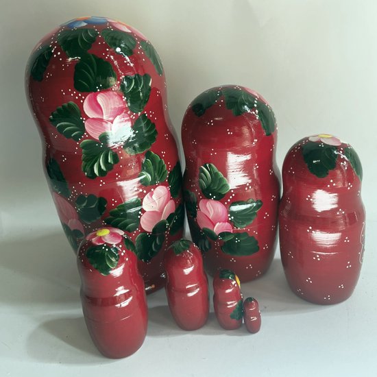 Een set van zes bordeauxrode Matroesjka poppen met een eenvoudige bloemmotief in roze en groen. De grootste pop is links.