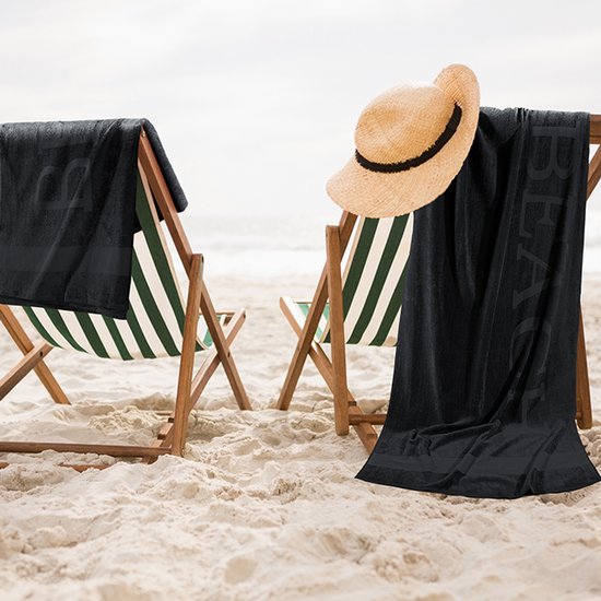 Twee ligstoelen op het strand met een zwarte handdoek met 'BEACH' erop.