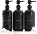 Drie natte, zwarte pompdispensers met schuim. Labels: BODY WASH, SHAMPOO, CONDITIONER.