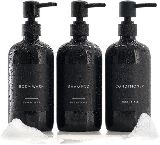 Drie natte, zwarte pompdispensers met schuim. Labels: BODY WASH, SHAMPOO, CONDITIONER.