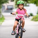 Meisje met een roze fietsbel met eenhoorn op een roze fiets met een groene helm.