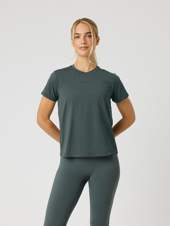Vrouw in een urban chic groen sportshirt met korte mouwen en een bijpassende legging, handen achter de rug.