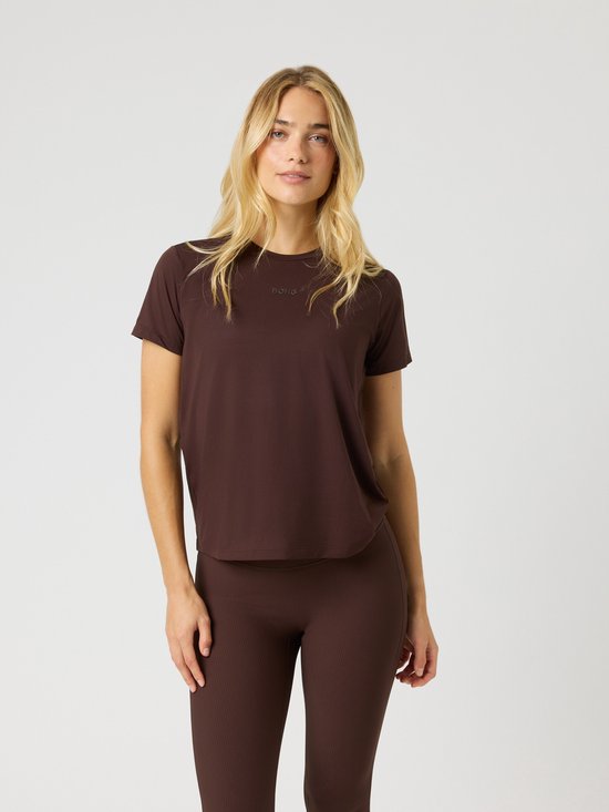 Femme blonde debout de face, vêtue d'un t-shirt de sport marron foncé à manches courtes et d'un legging assorti.
