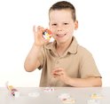 Jongen in beige poloshirt houdt een handgemaakte Bluey gipsfiguur omhoog, omringd door verfpotjes en gipsfiguren.