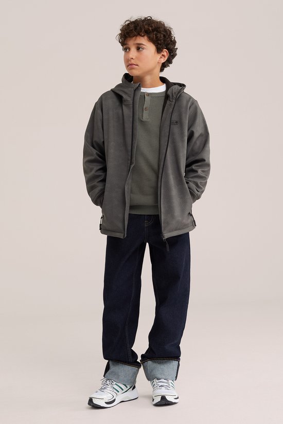 Jongen in grijze softshell jas met capuchon en subtiel ruitpatroon. Draagt groene trui en spijkerbroek.