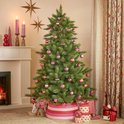 Versierde Triumph Tree kerstboom in een woonkamer met roze kerstballen en gestreepte mand.