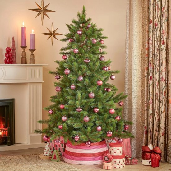 Versierde Triumph Tree kerstboom in een woonkamer met roze kerstballen en gestreepte mand.