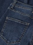 Detail van een donkerblauwe spijkerbroek met twee achterzakken en bruine stiksels.