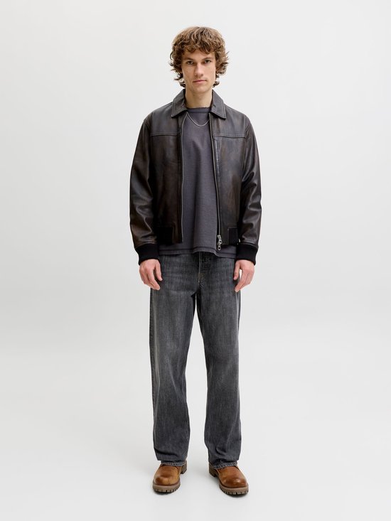 Model in een bruin leren jack en grijze jeans.