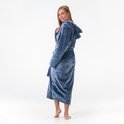 Femme en long peignoir bleu à capuche, se retourne. Douce sourire, main près du cou.
