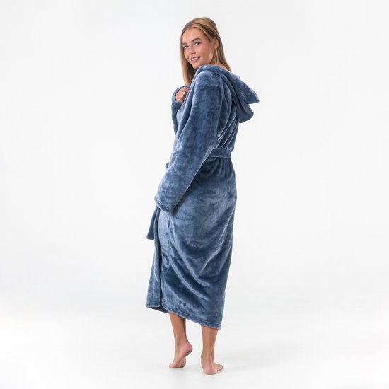 Femme en long peignoir bleu à capuche, se retourne. Douce sourire, main près du cou.