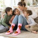 Vrolijke moeder met drie kinderen op de grond, allen met roze sokken met 'SUPER MOM' logo.