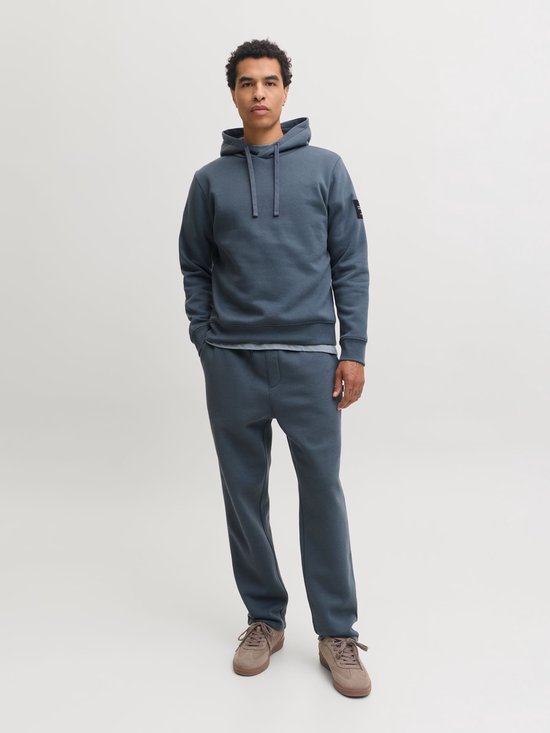 Man in een donkerblauwe joggingbroek met trekkoord en een bijpassende hoodie, sneaker.