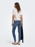 Vrouw in blauwe skinny jeans met lichte wassing, rafelige zoom en witte top.